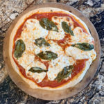 4 ingredient margherita pizza on a marble counter and pizza stone
