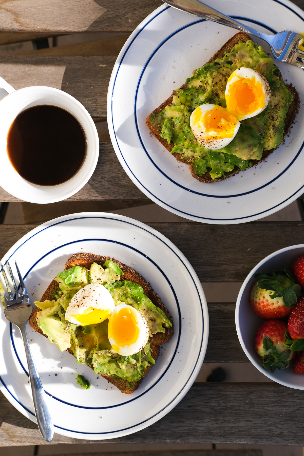plates of avocado toast with soft boiled eggs and strawberries for breakfast
