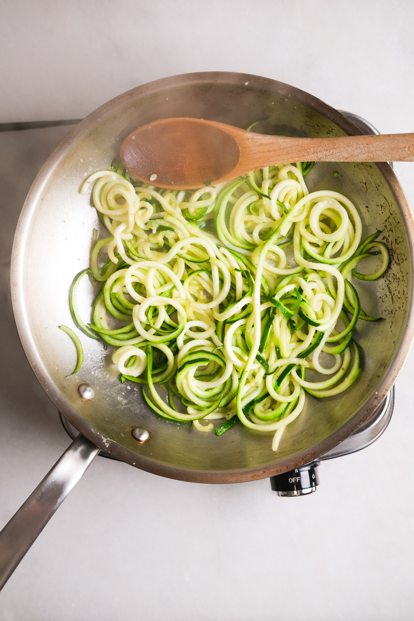 cooking zoodles in a skillet with a wooden spoon