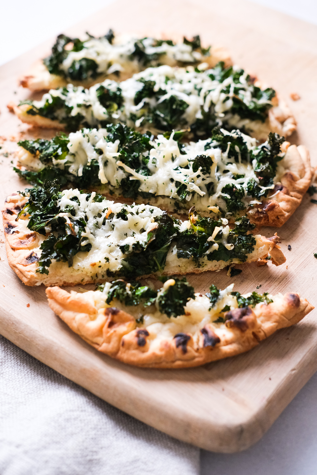 close up of kale parmesan flatbread slices on a cutting board