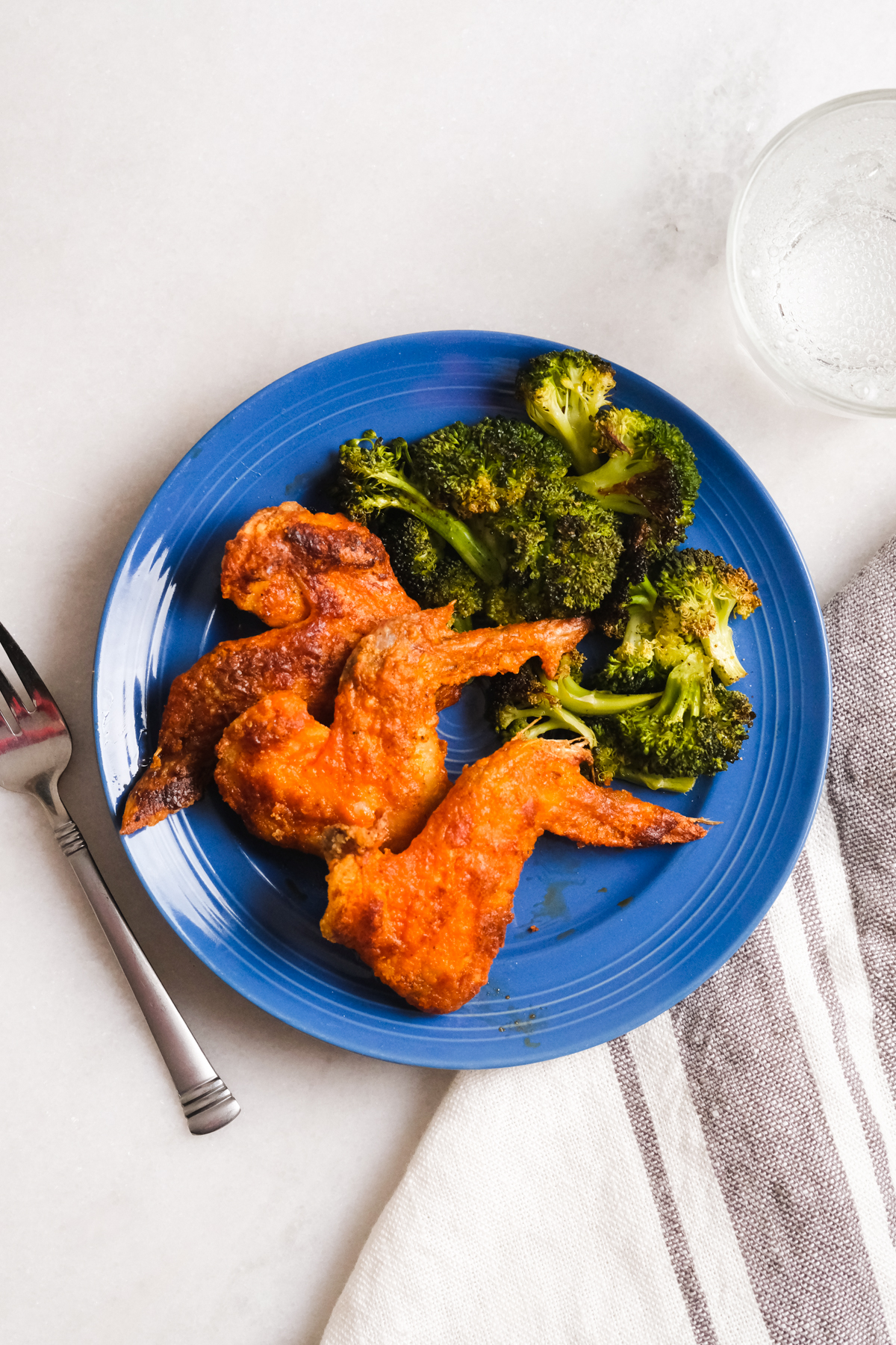 crispy oven baked buffalo wings on a blue plate with broccoli