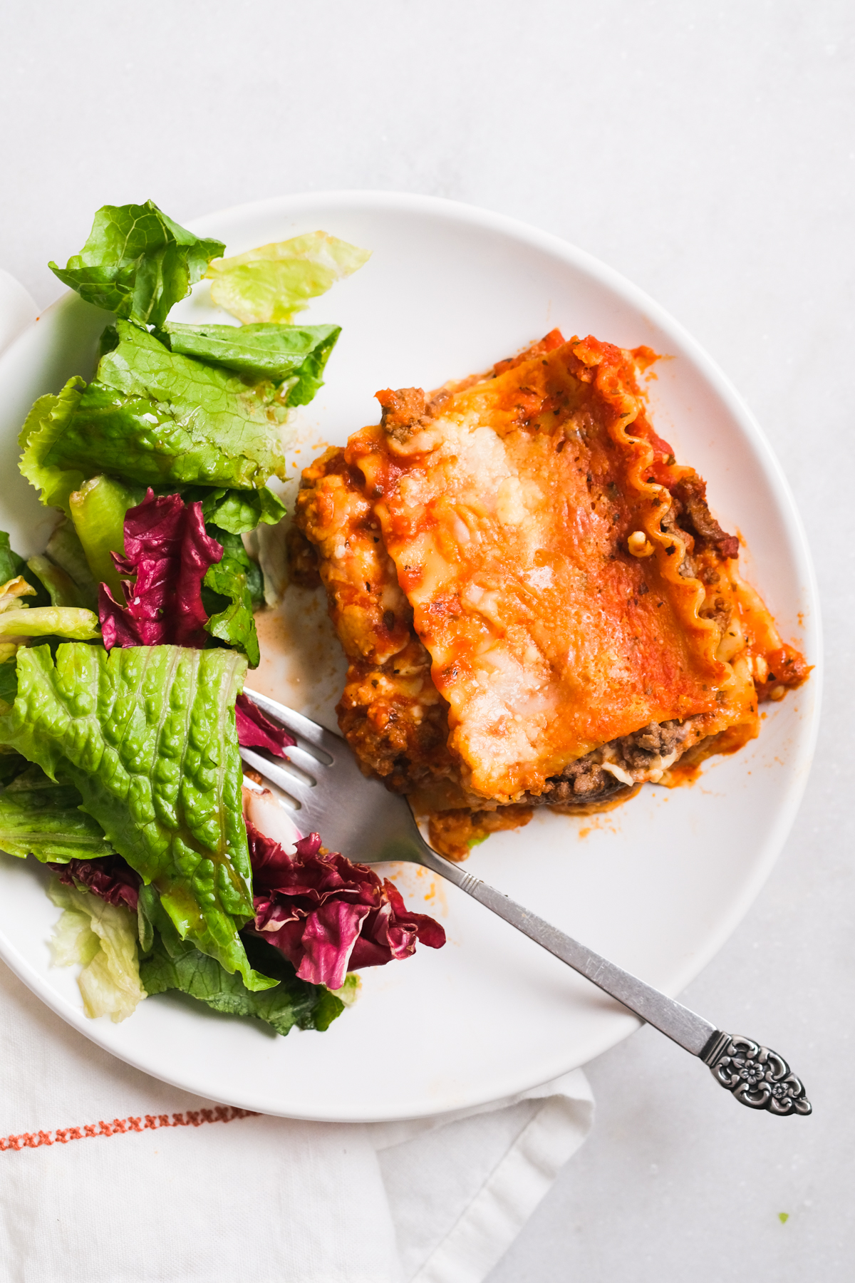 slice of cottage cheese lasagna with side salad on a white plate