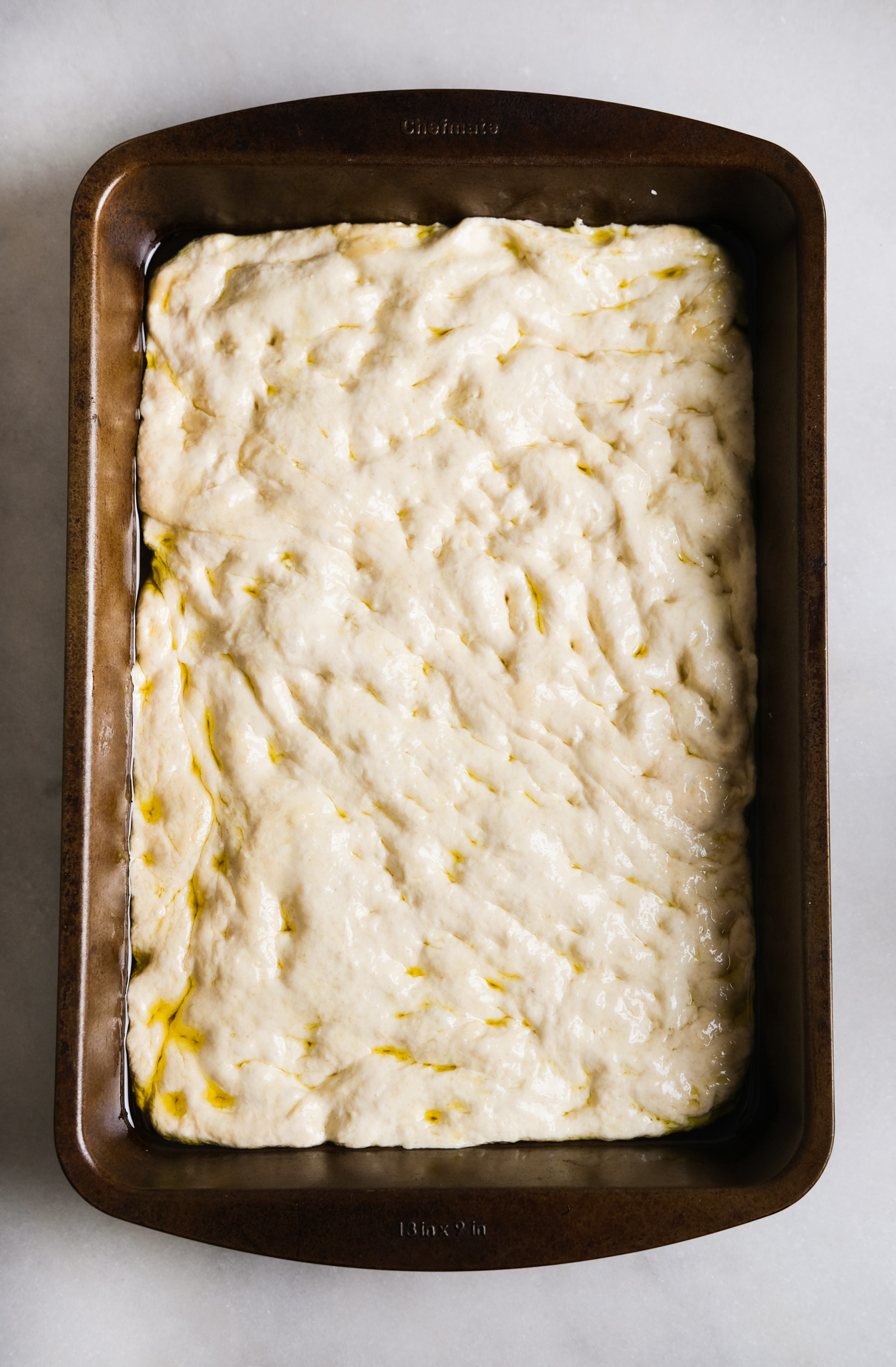 pressing into focaccia dough in a baking sheet with olive oil