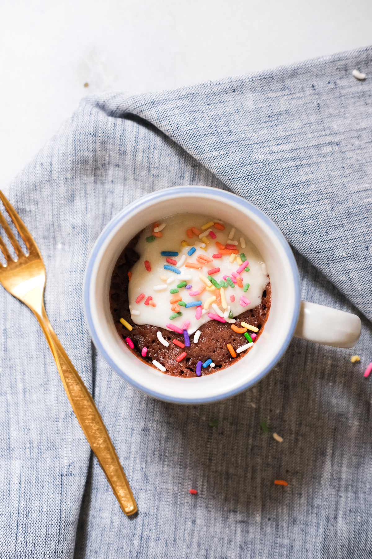 chocolate mug cake with vanilla frosting and rainbow sprinkles