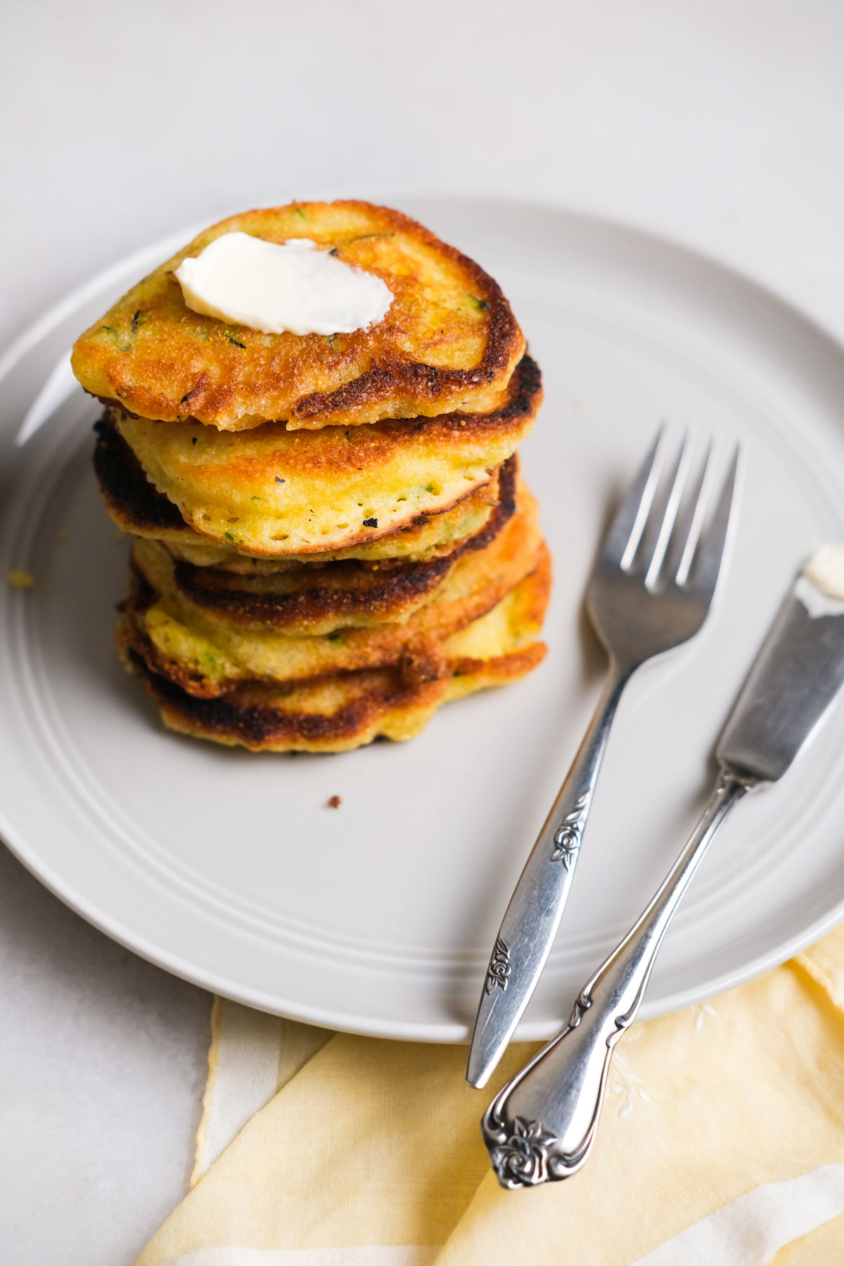 zucchini fritters stacked on a plate with spreadable butter