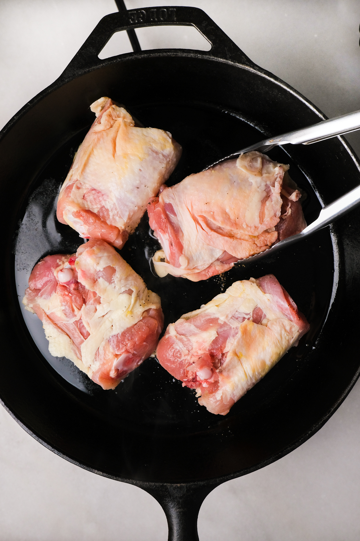 adding chicken thighs to a cast-iron skillet