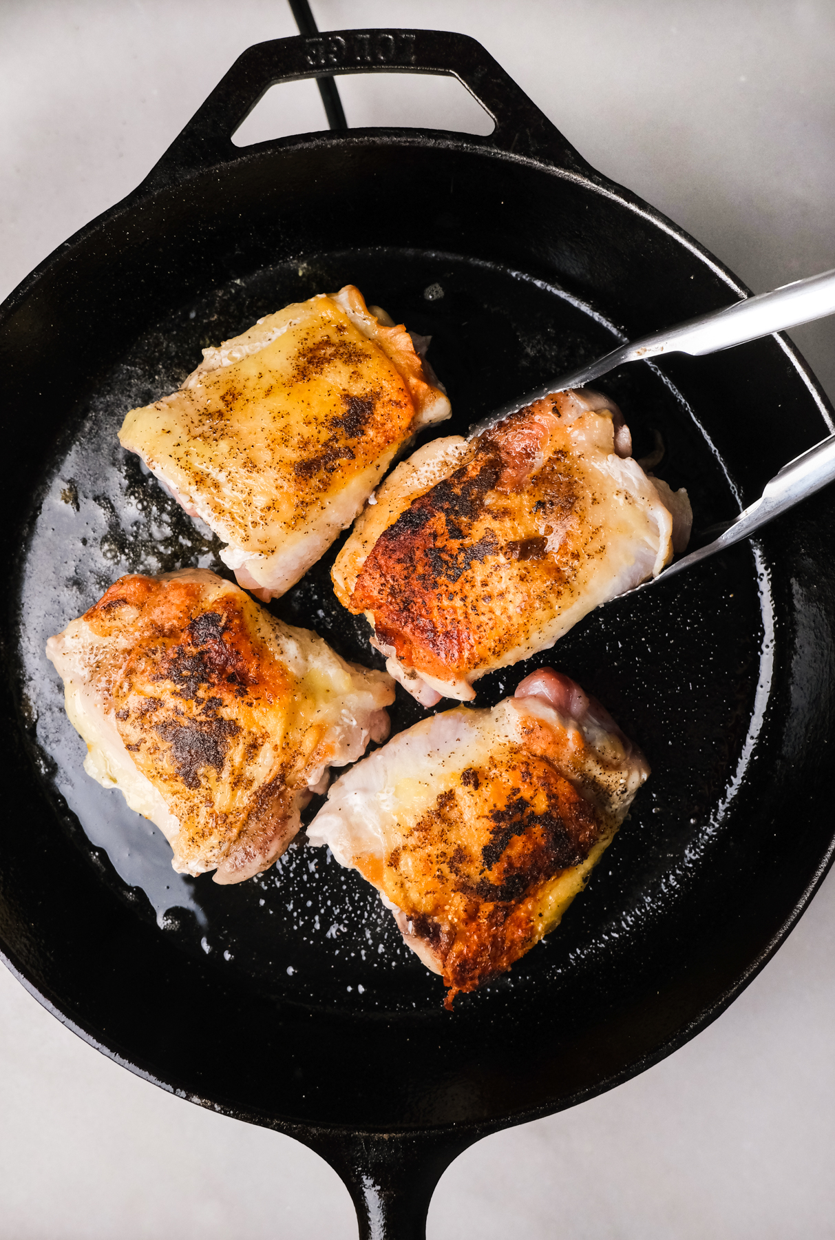 flipping chicken thighs in a cast iron skillet with tongs