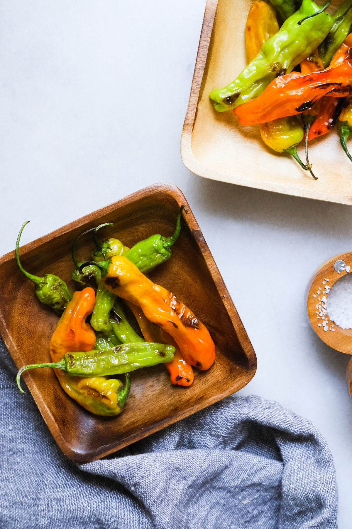 blistered shishito peppers in bowls with flaky sea salt