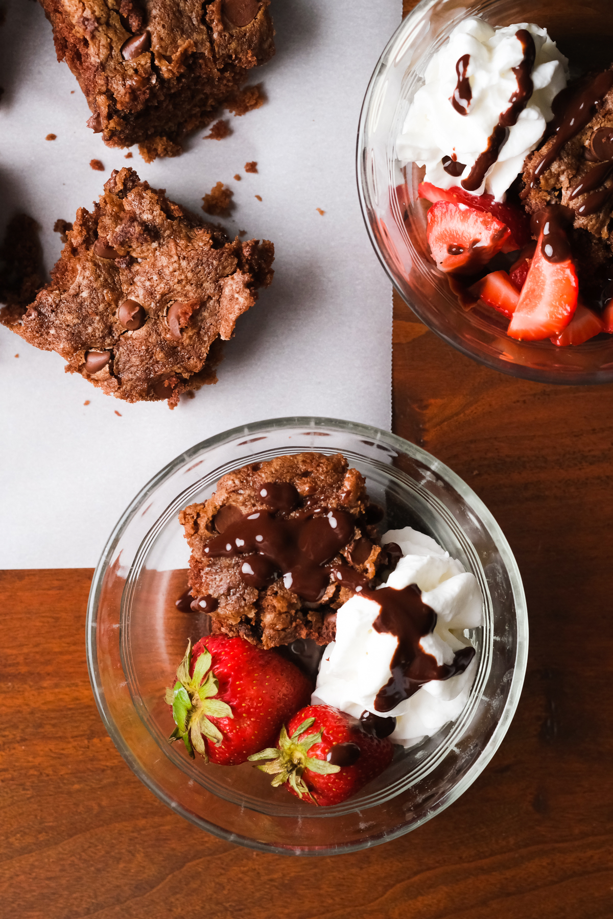 zucchini brownie in a bowl with whipped cream strawberries and chocolate sauce