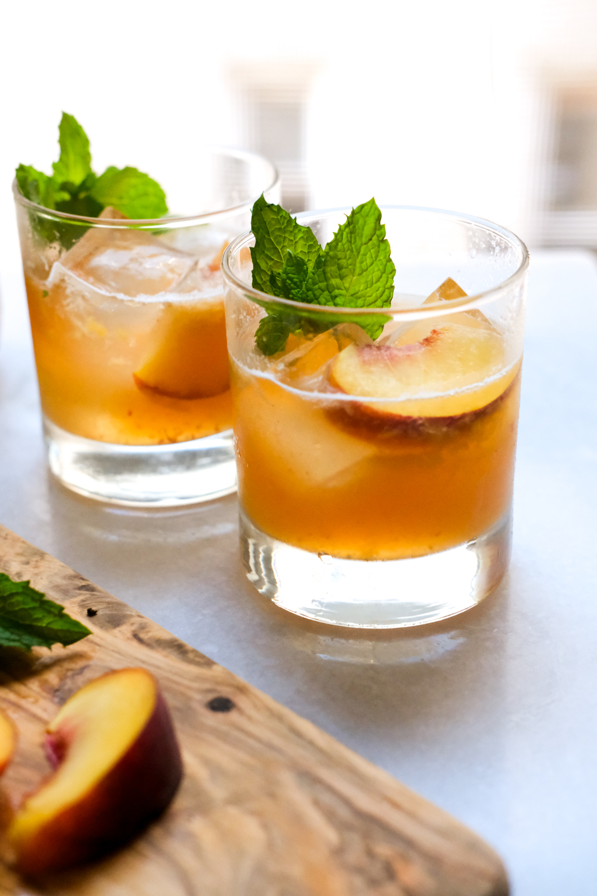 two peach bourbon smash cocktails on the counter