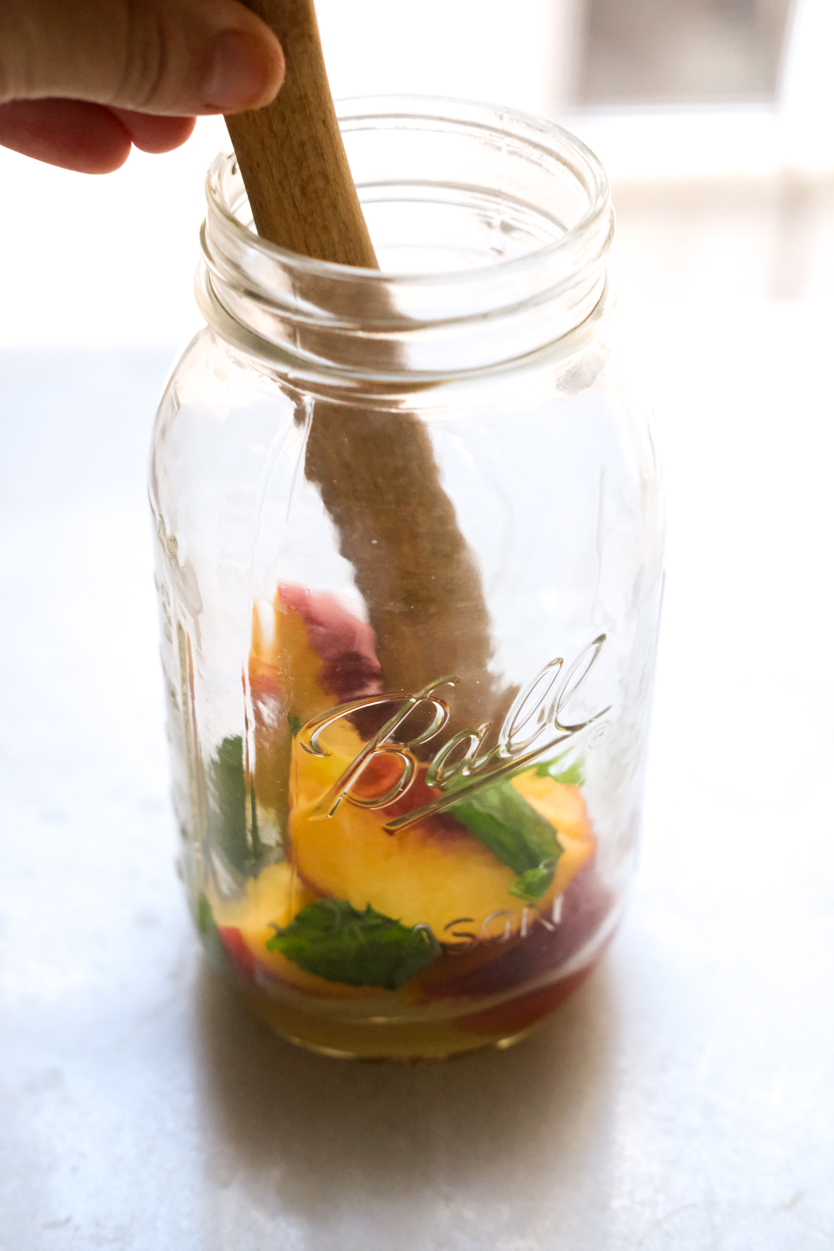 muddling peach slices and mint with lemon for a cocktail