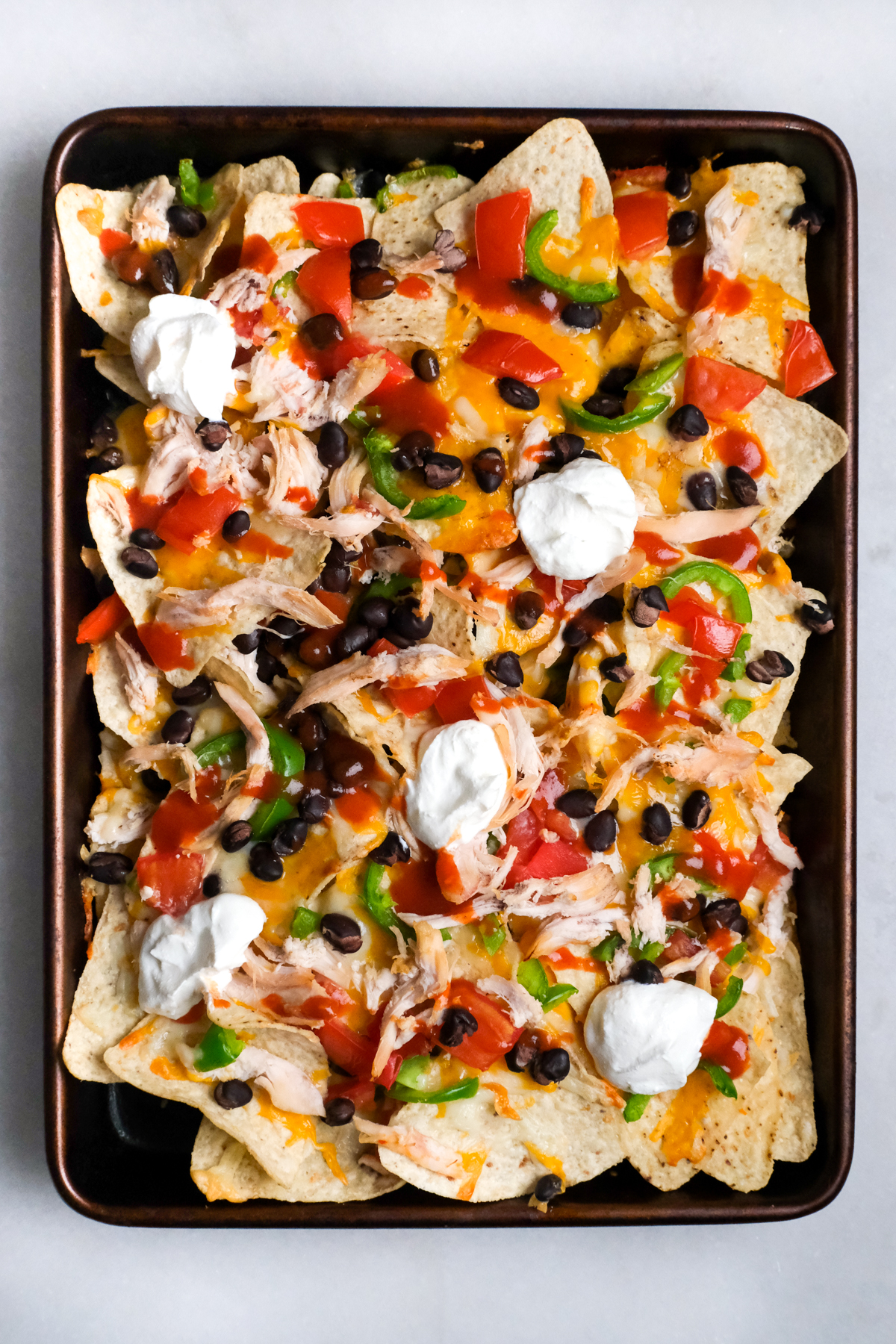 sheet pan with chicken nachos topped with fixings and sour cream