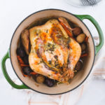 dutch oven roast chicken with herbs and potatoes and carrots on a table