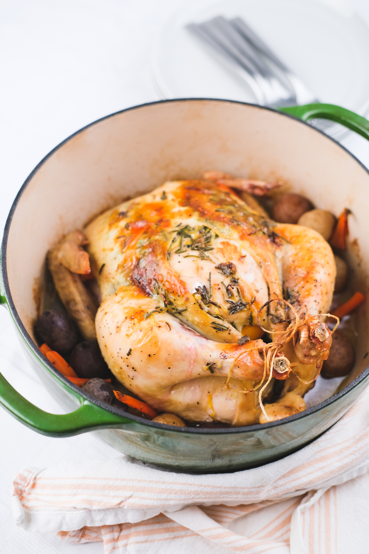 dutch oven roast chicken with herbs and butter surrounded by potatoes and carrots
