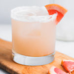 mezcal paloma cocktail on a board with grapefruit wedges and a salt rim