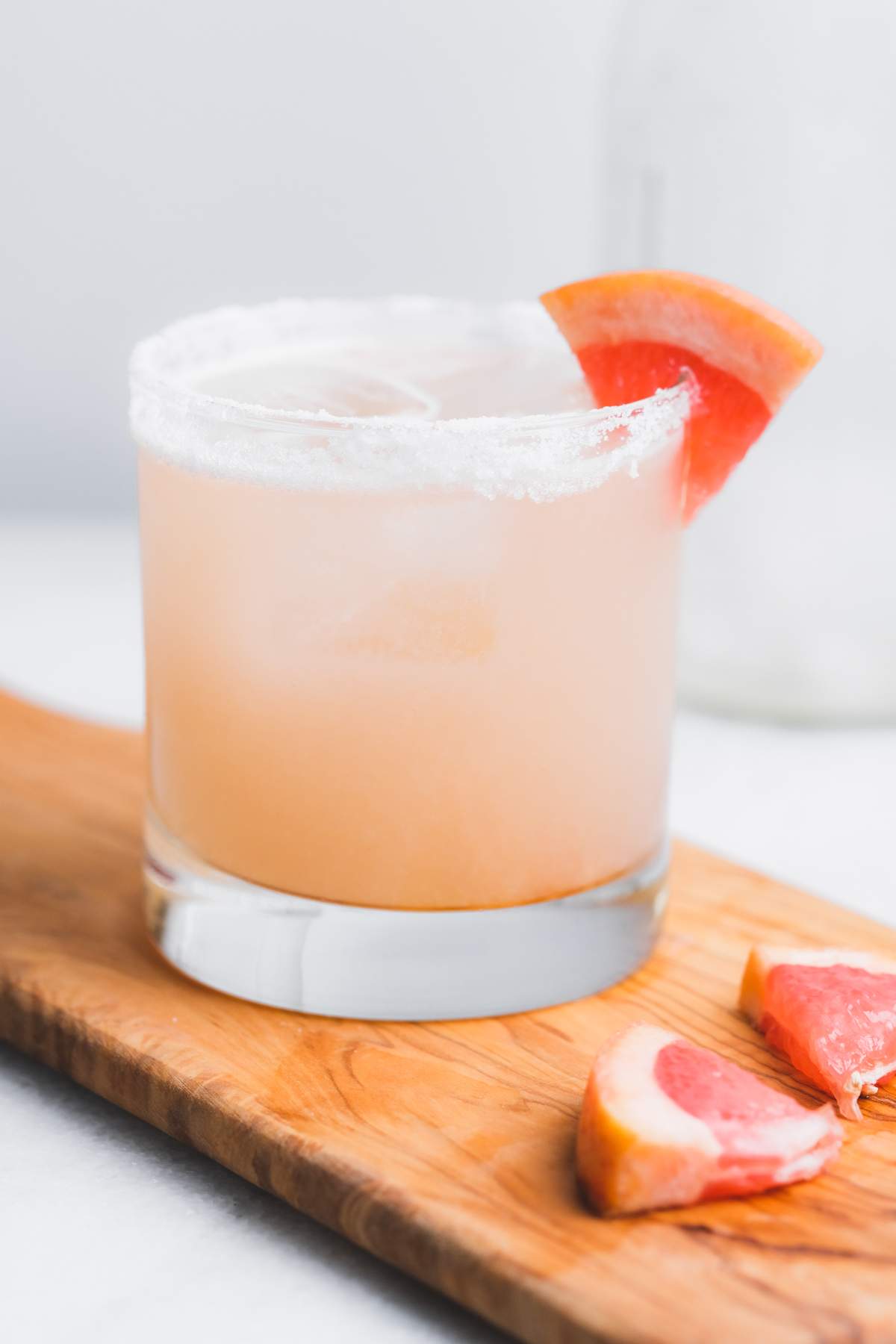 mezcal paloma cocktail on a board with grapefruit wedges and a salt rim