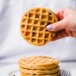 holding a mini chocolate chip oat waffle above a stack on a plate