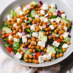 roasted chickpea greek salad in a grey bowl with dressing container on the side