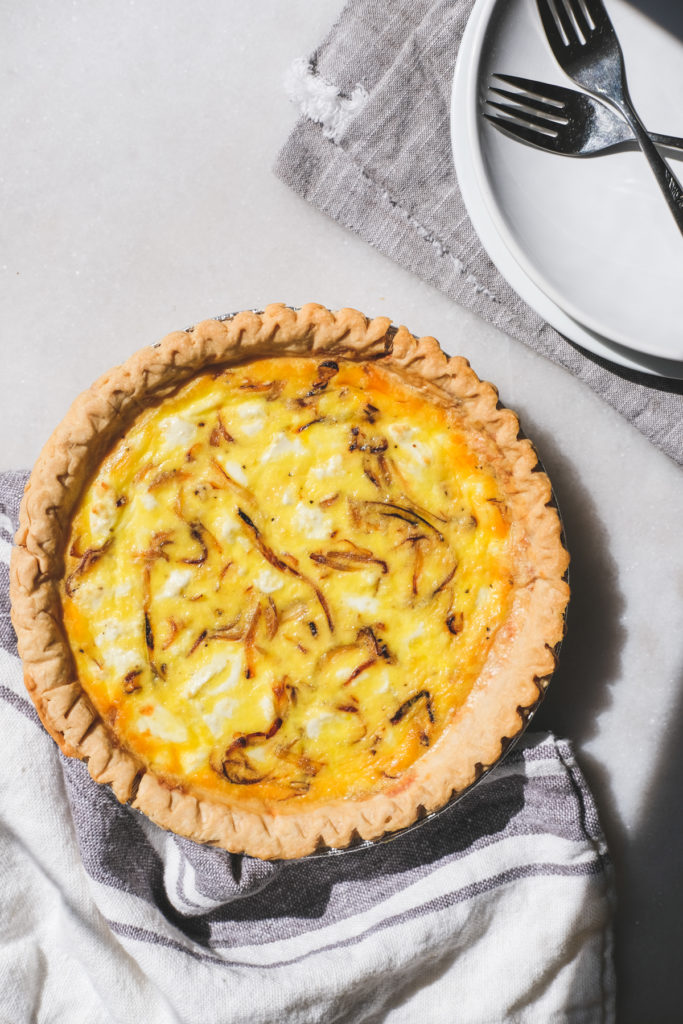 caramelized onion and goat cheese quiche on a breakfast table with plates and forks