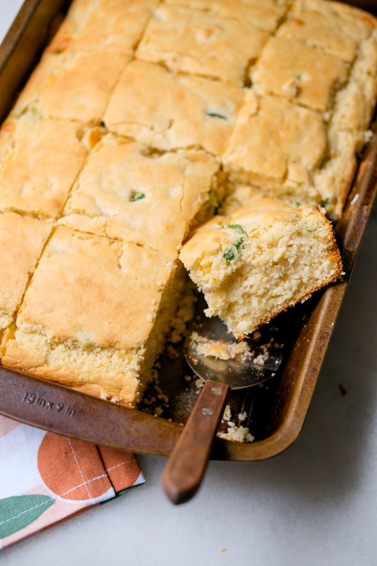 slicing up a jalapeno cheddar cornbread in a 9x13 pan