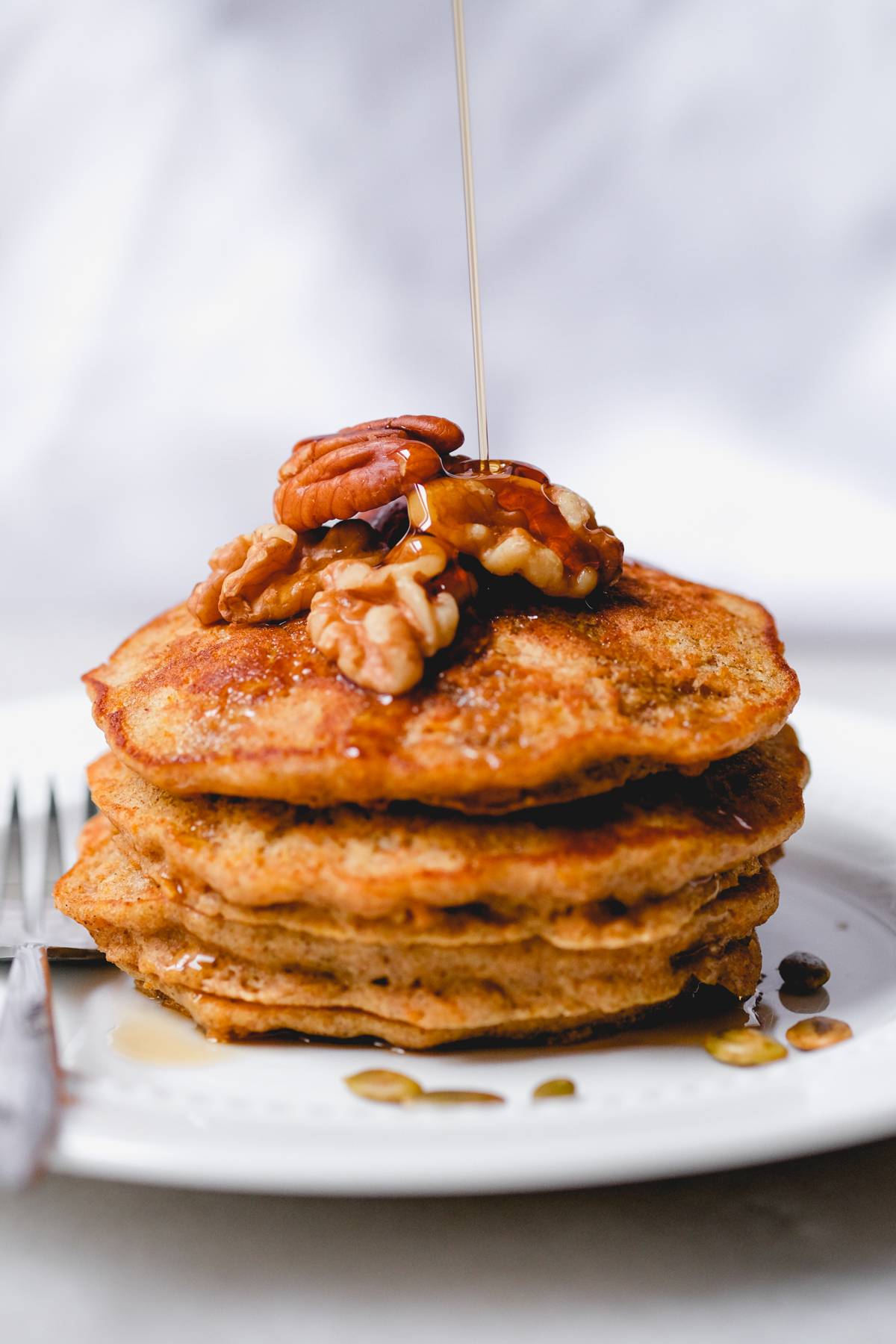 short stack of carrot cake pancakes with nuts on top with a drizzle of maple syrup