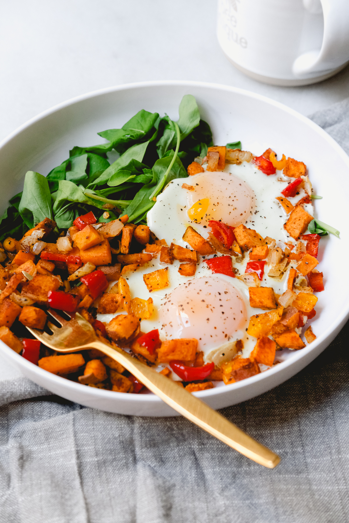 roasted sweet potato hash with eggs in a bowl with arugula