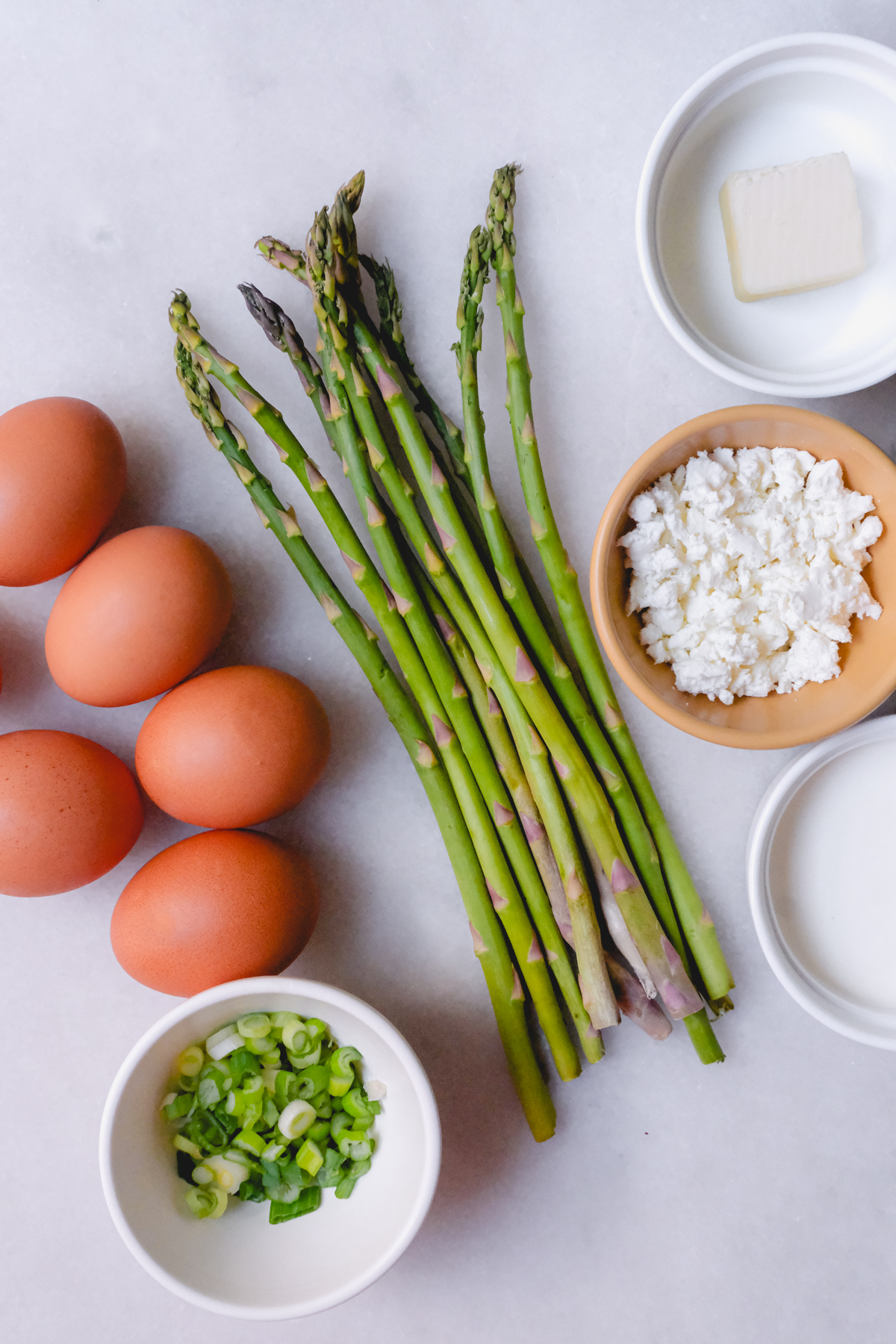 ingredients needed for a spring green onion asparagus frittata including eggs, asparagus, goat cheese, butter, and milk.
