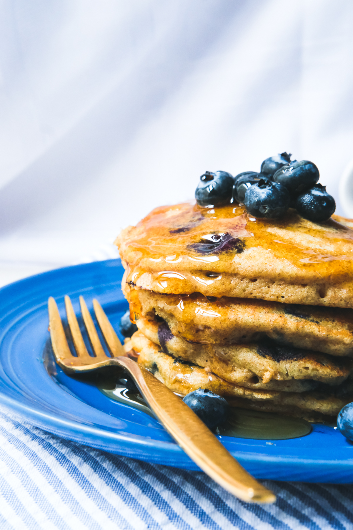 single stack of whole wheat blueberry pancakes with syrup on a blue plate